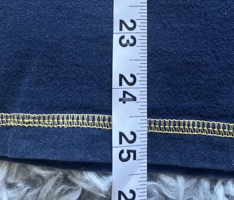 K&ouml;nnte beinhalten: Nahaufnahme eines marineblauen Stoffes mit gelbem Saum. Ein Lineal wird vertikal entlang des Stoffes platziert und zeigt Messungen von 58 bis 63 cm.