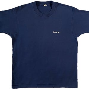 May include: A navy blue short-sleeve t-shirt with the word "BOSCH" printed in white on the front. The shirt has a crew neck and a simple, classic design, suitable for casual wear.
