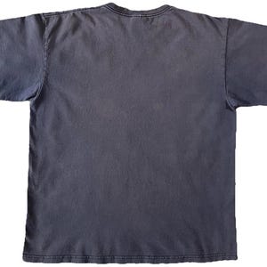 May include: A faded charcoal gray t-shirt with short sleeves. The shirt has a crew neck and a slightly worn appearance, suggesting it has been washed. The fabric appears soft and comfortable, suitable for casual wear.