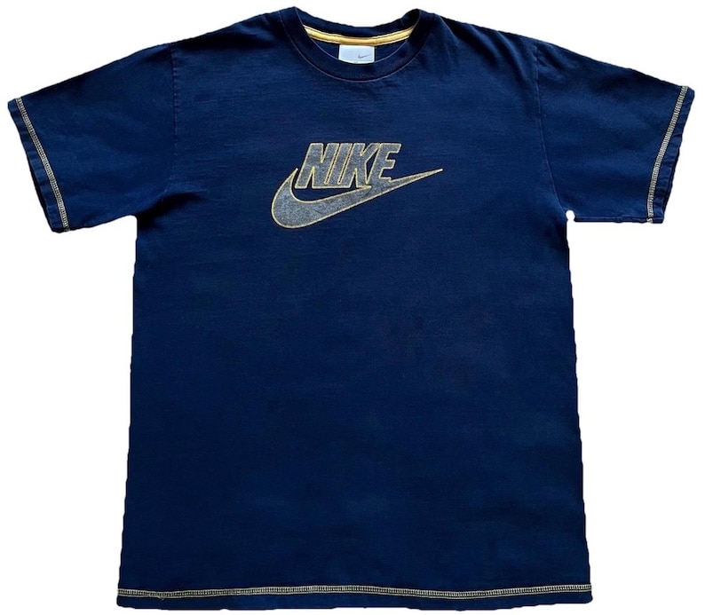 K&ouml;nnte beinhalten: Marineblaues T-Shirt mit goldenem Nike-Logo und Swoosh. Das Shirt hat goldfarbene N&auml;hte an &Auml;rmeln und Saum. Der Kragen ist mit Gold verziert. Kleines Nike-Logo am Kragen.