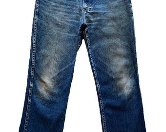 May include: A pair of medium-wash blue denim jeans featuring a classic five-pocket design, a metal button closure at the waist, a zippered fly, and visible fading on the thighs and knees, showcasing a straight-leg cut and sturdy stitching.