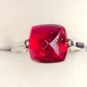 Op de afbeelding: Een zilveren ring met een grote, vierkante, rode edelsteen.