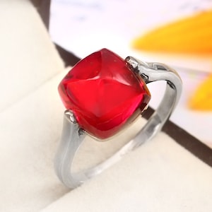 Op de afbeelding: Een zilveren ring met een grote, vierkante, rode edelsteen.