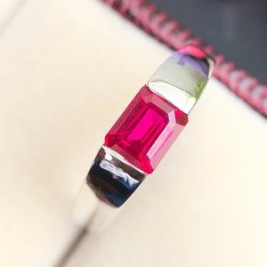 May include: A silver ring with a bright red emerald-cut gemstone.