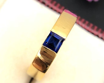 May include: A gold band ring with a square blue sapphire gemstone.
