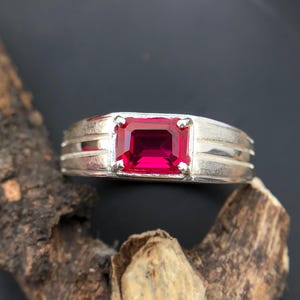Könnte beinhalten: Ein silberner Ring mit einem leuchtend roten rechteckigen Edelstein.