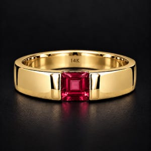 Puede incluir: Un anillo de banda de oro amarillo de 14K pulido con una piedra preciosa roja vibrante de corte cuadrado engastada en el centro. El interior de la banda está claramente grabado con el texto 14K, indicando la pureza del oro de esta joya.