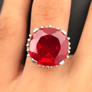 May include: A silver ring with a large, red, faceted gemstone set in a decorative, scalloped bezel.