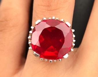 May include: A silver ring with a large, red, faceted gemstone set in a decorative, scalloped bezel.