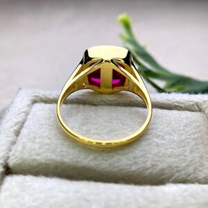 May include: A gold ring featuring a large, rectangular, vibrant pink gemstone. The ring's band and setting are a polished gold color, with a simple, elegant design. The gemstone is the focal point, catching the light and drawing the eye.