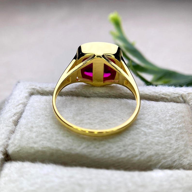 May include: A gold ring featuring a large, rectangular, vibrant pink gemstone. The ring's band and setting are a polished gold color, with a simple, elegant design. The gemstone is the focal point, catching the light and drawing the eye.