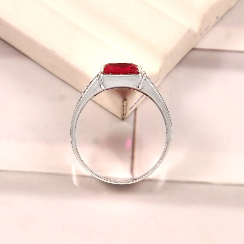 May include: A silver ring with a large, red, square-shaped gemstone. The ring has a simple band with a small, decorative detail on the side.