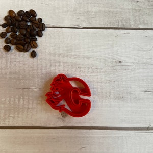 Könnte beinhalten: Roter Plastik-Ausstecher in Form des Buchstabens "C" mit Flammen darum.