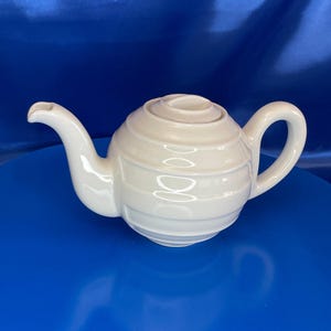May include: A white ceramic teapot with a rounded body and a ribbed design. The teapot has a spout and a handle.