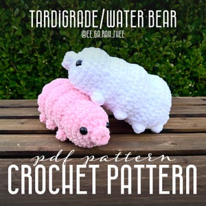May include: Two crocheted plush toys shaped like tardigrades, also known as water bears. The toys are pink and white and have black eyes. The text "pdf pattern CROCHET PATTERN" is at the bottom of the image.