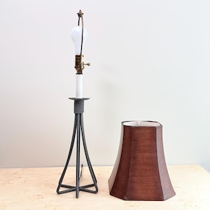 May include: A table lamp with a dark gray metal tripod base and a central white column. The lamp features a brass socket with a pull chain and a white light bulb. Beside the lamp base sits a separate, flared, dark brown textured lampshade.
