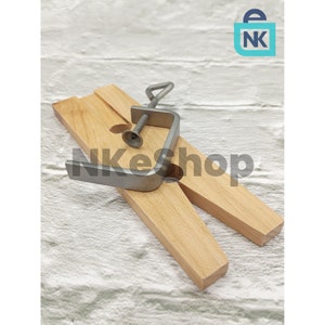May include: A wooden clamp with a metal screw and a metal handle. The clamp is made of two pieces of wood that are joined together by a metal screw. The handle is attached to the screw and can be used to tighten the clamp.