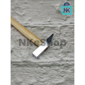 May include: A small hammer with a wooden handle and a silver metal head. The hammer is lying on a light brown textured surface.