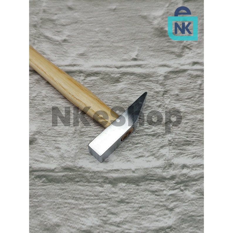 K&ouml;nnte beinhalten: Ein kleiner Hammer mit einem Holzstiel und einem silbernen Metallkopf. Der Hammer liegt auf einer hellbraunen, strukturierten Oberfl&auml;che.