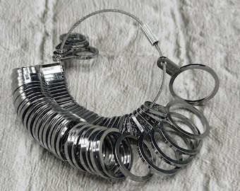 May include: A silver ring sizer with a chain and a clasp. The sizer is made up of a series of graduated rings that can be used to determine the size of a ring.