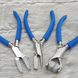 May include: A set of three metal pliers with bright blue rubberized handles. The left pair features flat white nylon jaws, the center pair has one round metal jaw and one flat white nylon jaw, and the right pair includes two grooved white nylon rollers.