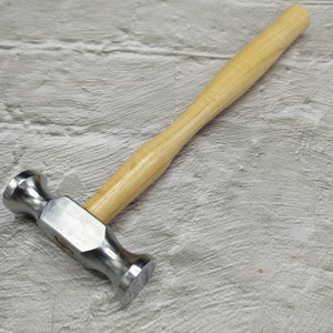 May include: A silver metal hammer with a wooden handle. The hammer has a rounded head and a flat face.