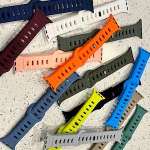 Op de afbeelding: Een verzameling kleurrijke siliconen horlogebandjes in verschillende tinten, waaronder rood, blauw, oranje en groen. De bandjes hebben een sleufontwerp voor verstelbaarheid en worden getoond op een lichtgekleurd oppervlak.
