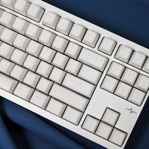 May include: A white mechanical keyboard with light gray keycaps. The keyboard has a standard layout with function keys, a number pad, and arrow keys. The background is a dark blue fabric.