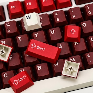 May include: Close-up of a mechanical keyboard with red and white keycaps. The keycaps are a deep red color, with white lettering. The "Shift" key is red with white text. The "W" key is white with black lettering. The keyboard is a modern design.