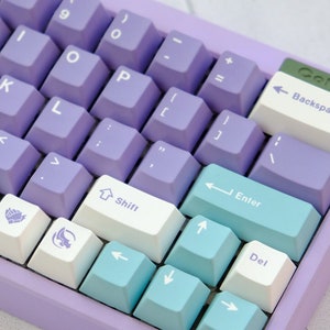 May include: A purple mechanical keyboard with white and blue keycaps. The keyboard has a variety of keys, including letters, numbers, symbols, and arrow keys. The keyboard also has a backspace key, an enter key, a shift key, and a delete key. The keyboard is on a white surface.