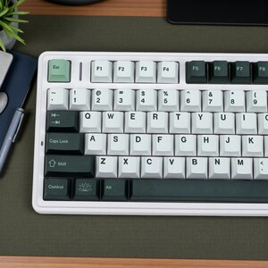May include: A white mechanical keyboard with light green and dark green keycaps. The keyboard has a standard QWERTY layout with function keys and a control section. The Esc key is light green, and the Shift key is dark green.