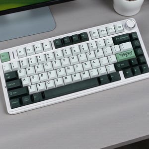 May include: A white mechanical keyboard with a variety of key colors, including white, black, and green. The keyboard has a volume knob and a layout with function keys. The keycaps feature standard letters, numbers, and symbols.