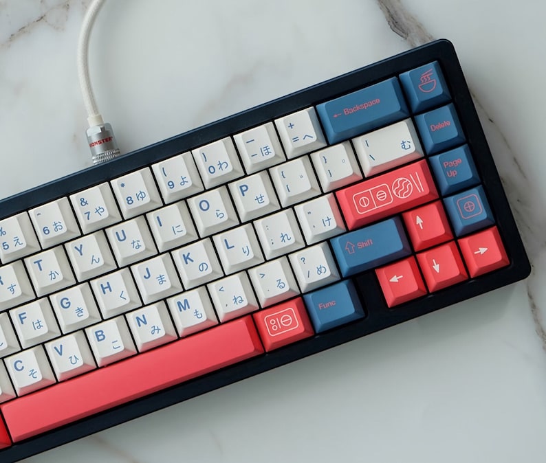 May include: A white and blue mechanical keyboard with Japanese characters on the keys. The keyboard has a red and white space bar and a black frame. The keyboard is connected to a white cable.