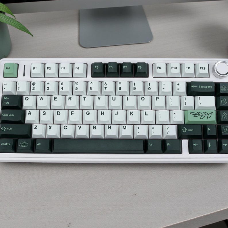May include: A white mechanical keyboard with black and green keycaps. The keyboard has a standard QWERTY layout with function keys and a volume control knob. The keycaps feature white lettering and green accent keys.