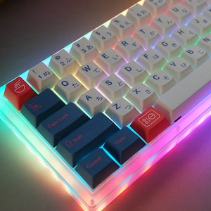 May include: A white mechanical keyboard with blue and red keycaps. The keyboard has a clear case with rainbow LED lighting. The keycaps have Japanese characters and symbols.