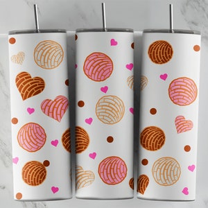 May include: Three white tumblers with a pattern of pink and brown concha pastries and pink hearts. The tumblers are on a white marble surface.