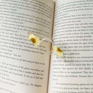 K&ouml;nnte beinhalten: Nahaufnahme eines Buches mit dem Text "Mommy Says" und "Dr. Shapiro Says." Das Buch ist ge&ouml;ffnet und ein Paar klarer herzf&ouml;rmiger Brillen mit getrockneten wei&szlig;en Blumen liegen auf den Seiten.
