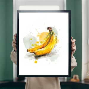 May include: A framed art print featuring a watercolor illustration of a bunch of ripe bananas. The bananas are yellow with brown tips, set against a backdrop of yellow and green watercolor splashes. The artwork is in a black frame.