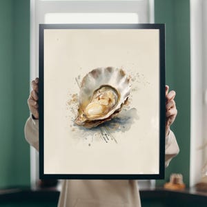 May include: A framed watercolour print of an oyster. The oyster is open, showing a creamy interior, with a shell in beige and brown hues. Beige and blue watercolour splatters surround the oyster, creating an artistic effect.