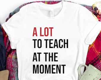 May include: White t-shirt with the text "A LOT TO TEACH AT THE MOMENT" in black and red lettering.