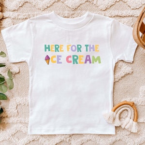 Pu&ograve; includere: Maglietta bianca con una grafica colorata che dice "Here for the Ice Cream" con un cono gelato disegnato.