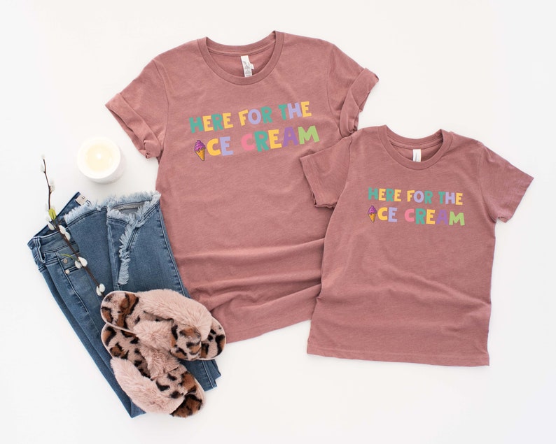 Pu&ograve; includere: Due magliette color malva con il testo "Here for the Ice Cream" in lettere colorate e un piccolo grafico di cono gelato.