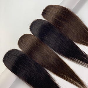 May include: A close-up of four hair extensions in varying shades of brown and black. The extensions are arranged in a row, showcasing the different color options available. The hair appears smooth and straight, with a natural shine.