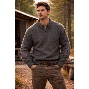 May include: A gray wool sweater with a button-up collar and elbow patches. The sweater is paired with brown pants and a brown leather belt. The background features a cabin and trees, suggesting an outdoor setting.