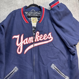 May include: A navy blue Yankees baseball jacket with a red and white trim. The word "Yankees" is embroidered in white script across the front. The jacket has a black quilted lining and black leather accents.