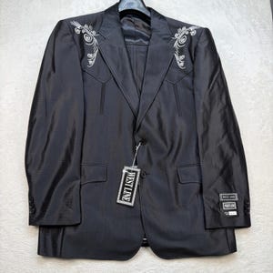 以下が含まれることがあります： 胸元のヨークに白い刺繍のスクロール模様が施された黒いブレザー。フロントは2つボタンで、袖口にはそれぞれ3つのボタンが付いています。フロントボタンにはWest Lineのブランドタグがぶら下がっており、左袖にもラベルが付いています。
