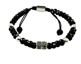 May include: Black beaded bracelet with silver accents and a central decorative cylinder. The bracelet features a sliding knot closure for adjustable sizing. The beads are faceted, reflecting light, and the overall design is sleek and modern.