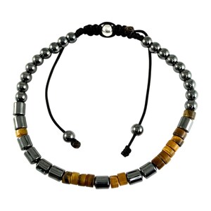 Könnte beinhalten: Verstellbares Armband mit einer Mischung aus dunkelgrauen, zylindrischen und kugelförmigen Perlen. Das Armband enthält natürliche Tigeraugen- und dunkelgraue zylindrische Perlen, die auf einem schwarzen Kordelband mit verstellbaren Enden aufgefädelt sind. In der Mitte befindet sich eine kleine silberne Perle.