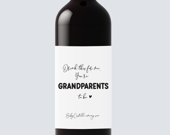 May include: A black wine bottle with a white label. The label reads "Drink this for me. You're GRANDPARENTS to be ♥ Baby Castillo coming soon."