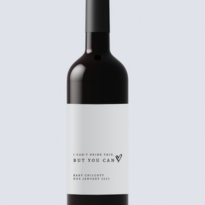 May include: A dark red wine bottle with a black top and a white label. The label reads "I CAN'T DRINK THIS, BUT YOU CAN" with a heart symbol, and "BABY CHILCOTT DUE JANUARY 2023".